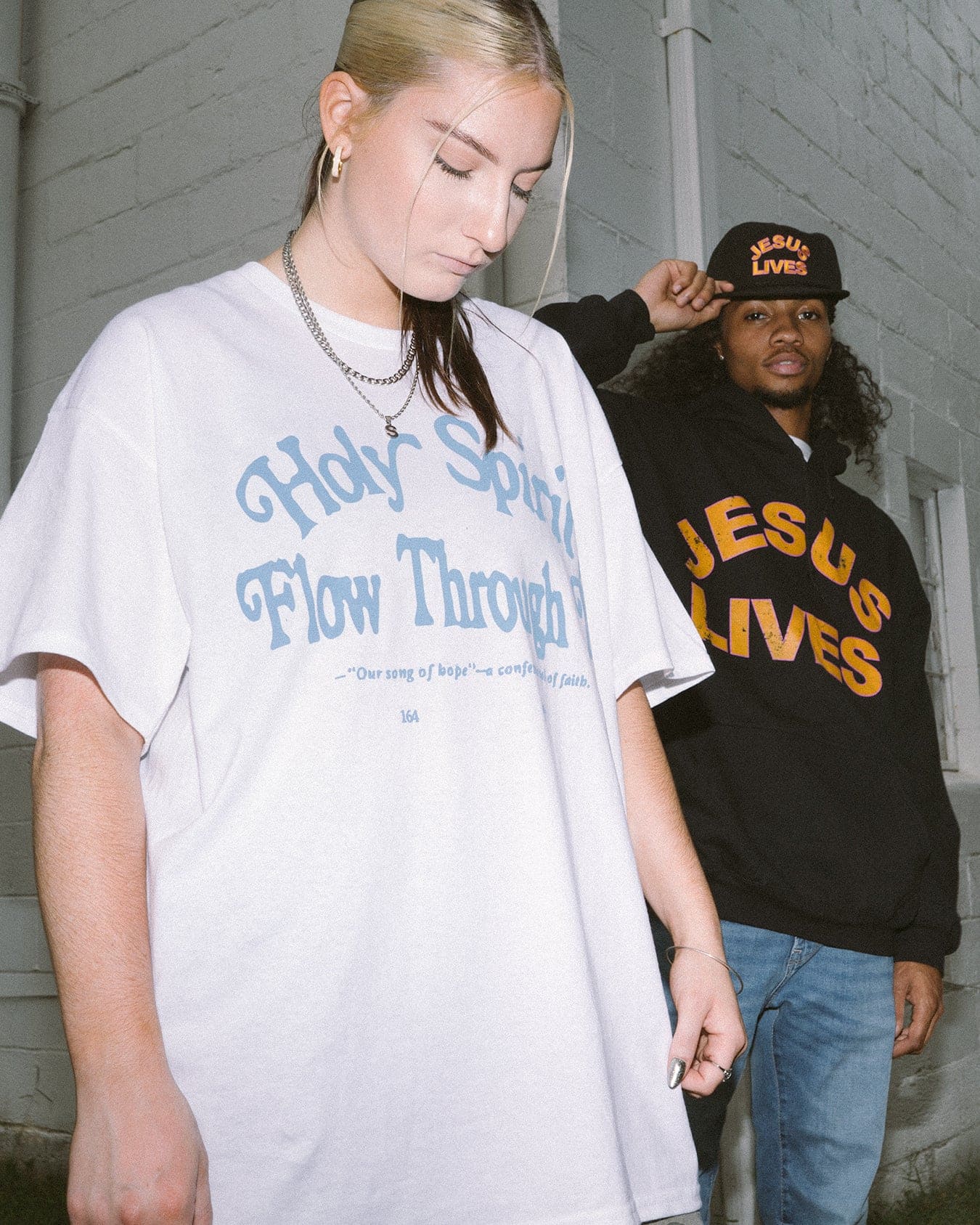 girl wearing white Holy Spirit flow through me christian t shirt with man wearing Jesus lives black hooded sweatshirt in front of a white brick building in Atlanta, Georgia
