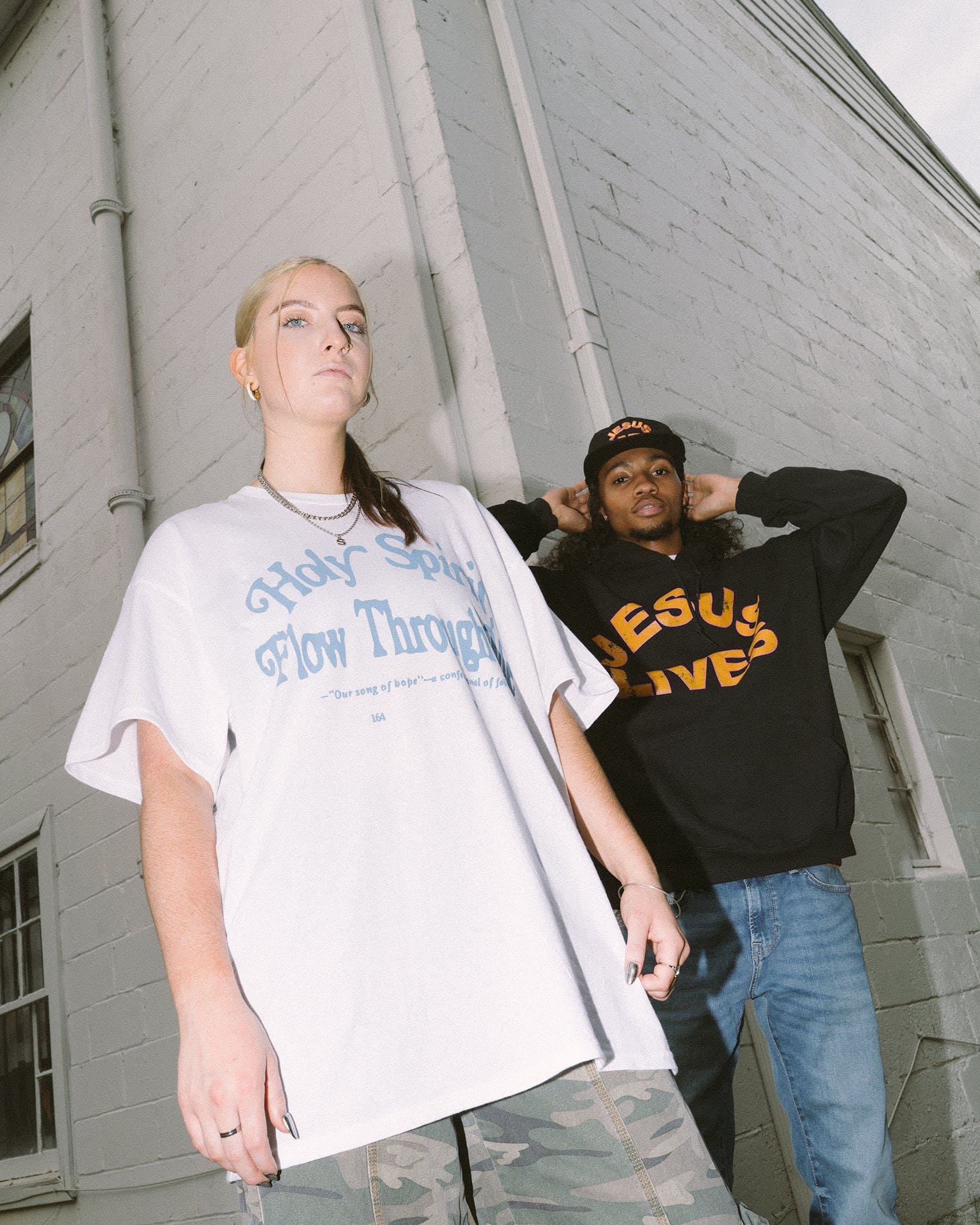 girl wearing white Holy Spirit flow through me christian t shirt with man wearing Jesus lives black hooded sweatshirt in front of a white brick building in Atlanta, Georgia