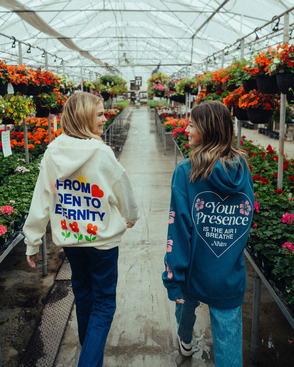 two women walking and smiling in a beautiful greenhouse full of flowers wearing NHIM Apparel christian sweatshirts