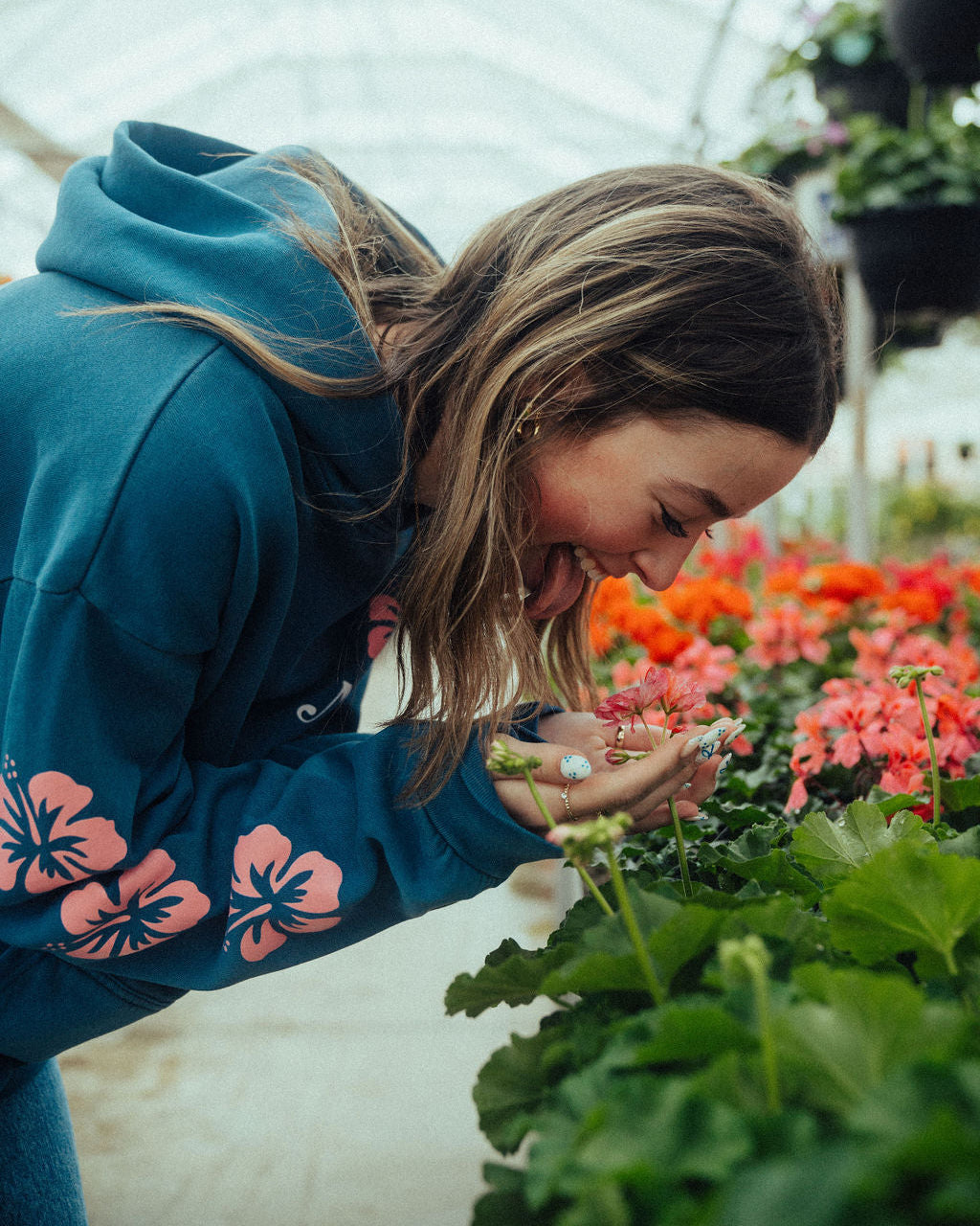 a women smiling looking at a flower in a beautiful greenhouse full of flowers wearing NHIM Apparel christian hoodie