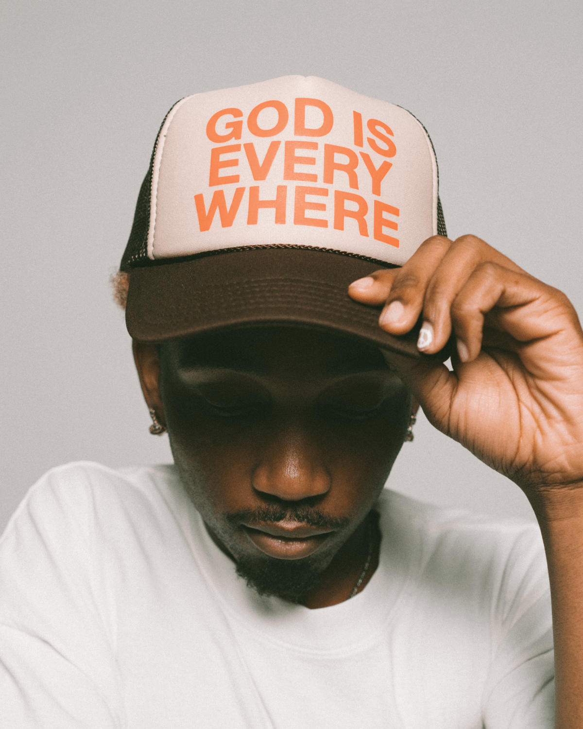 GOD IS EVERYWHERE Trucker hat brown and tan with orange writing. Christian hat by NHIM APPAREL. model portrait holding hat