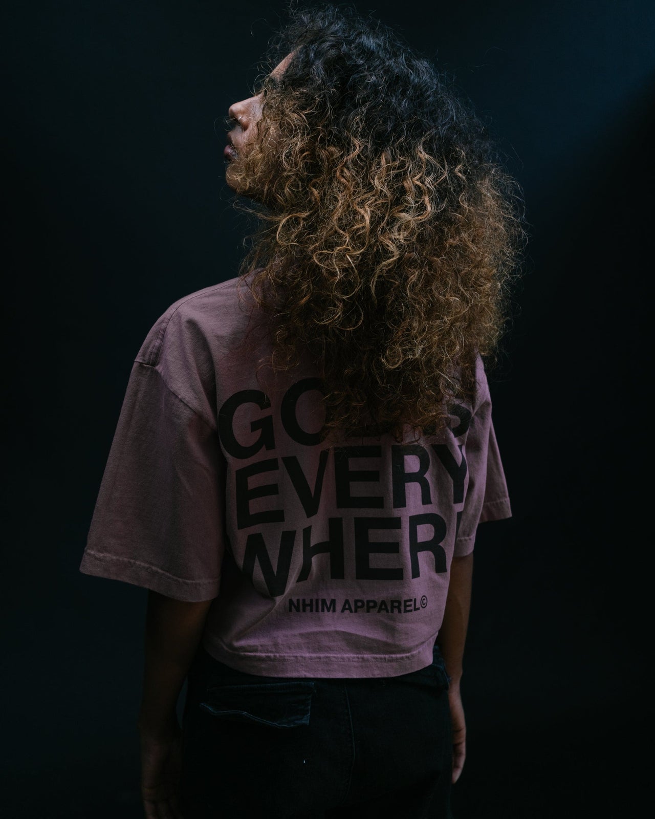 God Is Everywhere crop tee thistle color model with black background standing pic from back by NHIM Apparel christian clothing brand  