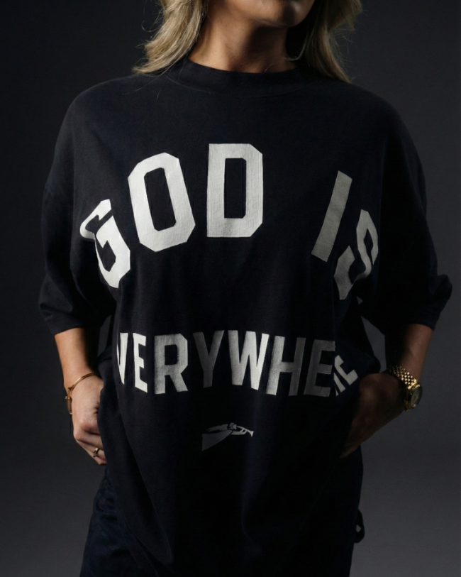 Person wearing a black sweatshirt with 'GOD IS EVERYWHERE' text on a dark background