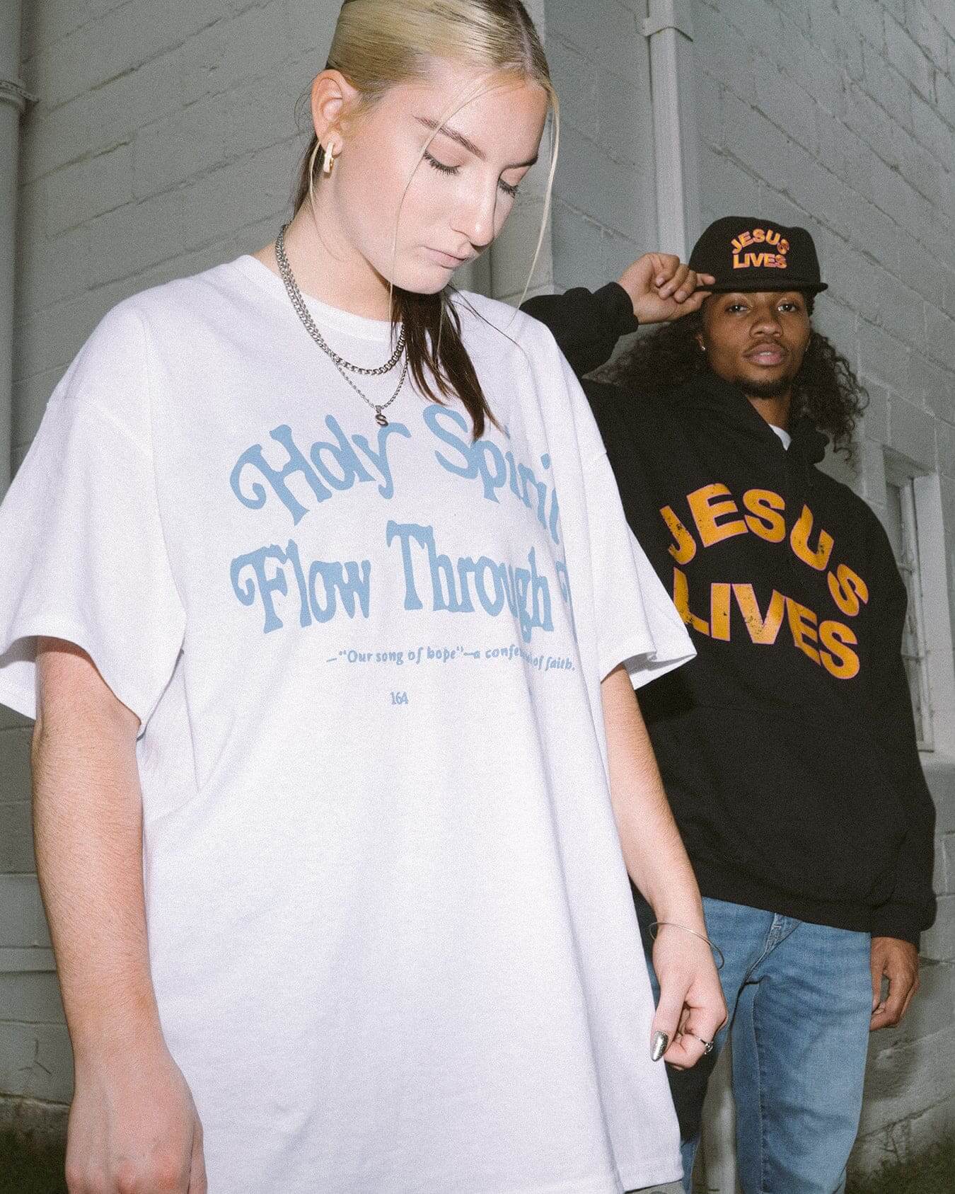 girl wearing white Holy Spirit flow through me christian t shirt with man wearing Jesus lives black hooded sweatshirt in front of a white brick building in Atlanta, Georgia