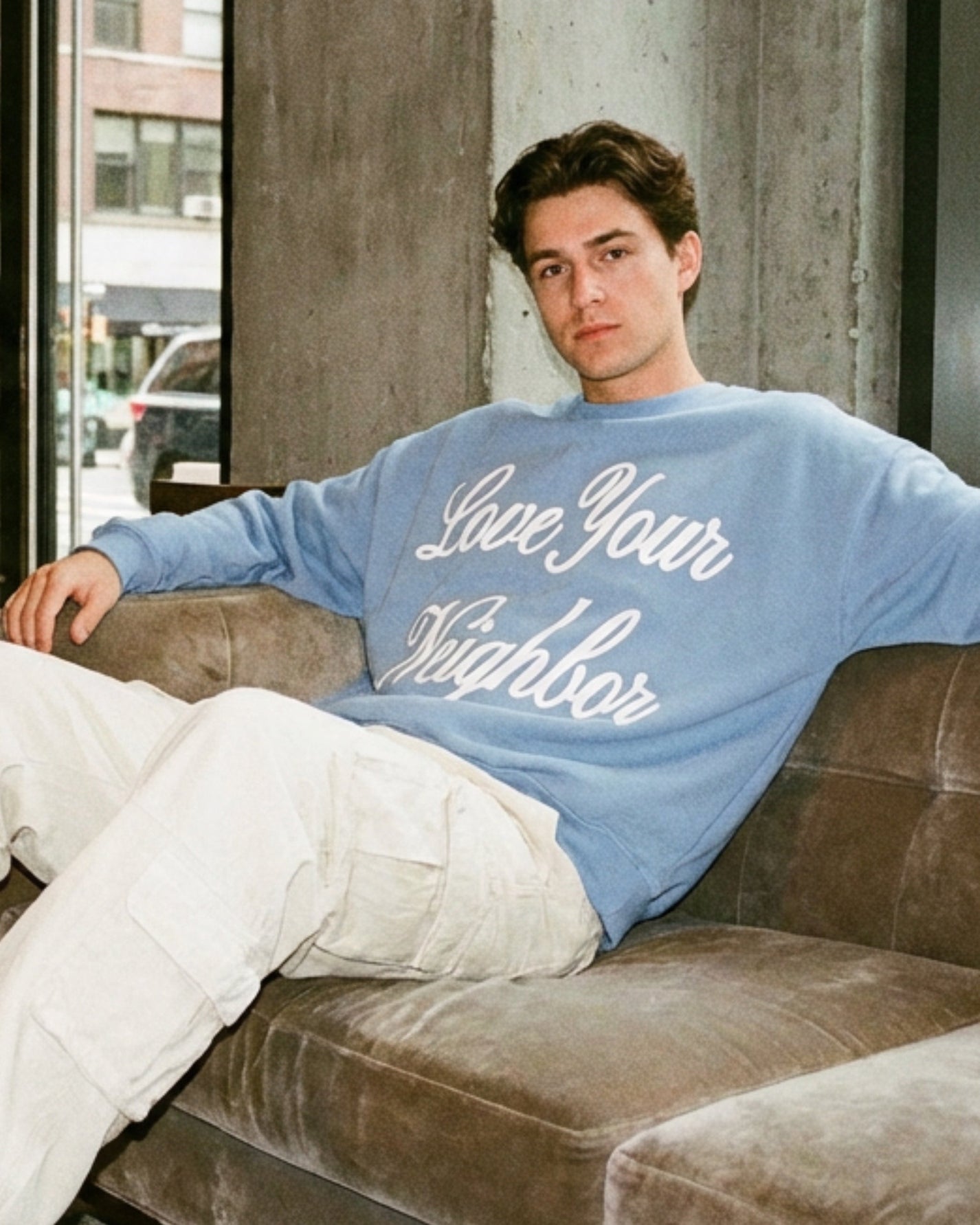 Man wearing a blue sweatshirt with 'Love Your Neighbor' text, sitting on a couch.
