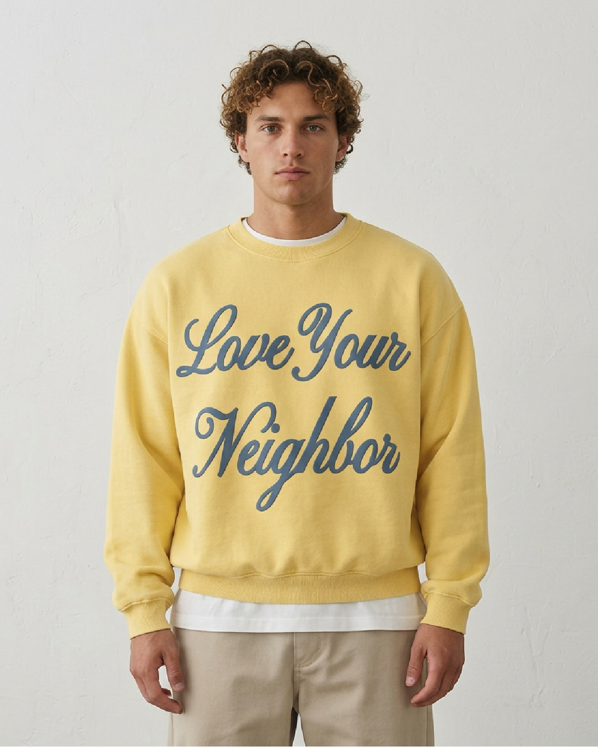 Man wearing a yellow sweatshirt with 'Love Your Neighbor' text on a plain background